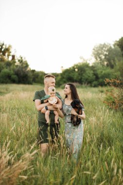 Sevimli kızlarıyla oynayan neşeli, genç ebeveynler ve köpekleri, bir çocuğun doğuşunun 6. ayını yeşil çayırın arka planında durarak kutluyorlar..