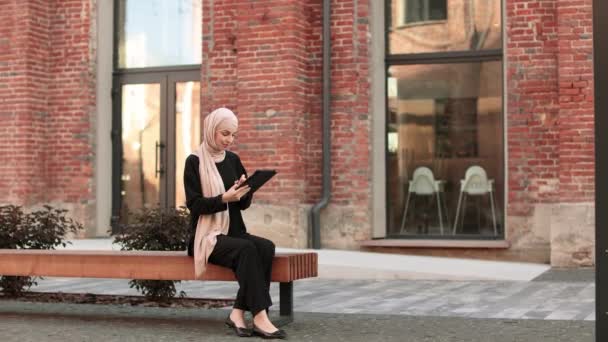 Całkiem Uśmiechnięta Muzułmańska Biznesmenka Hidżabie Siedzi Ławce Używa Tabletu Podczas — Wideo stockowe