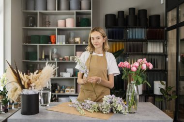 Woman florist at her own floral shop taking care of flowers. People, business, sale and floristry concept. Happy smiling florist woman making violet flower bunch at flower shop
