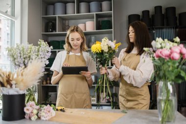 Çiçekçi dükkanında elinde tabletle iki mutlu çağdaş çiçekçi kızın portresi internetten video dersleri izlerken enfes bir buket yapıyor..