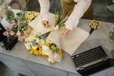 Çiçekçi ellerinin farklı çiçeklerden güzel bir buket yapıp tezgahta kurdele bağladığı kesikli manzarayı kapatın. Modern bayan çiçekçi dükkanda bir iş günü geçiriyor..