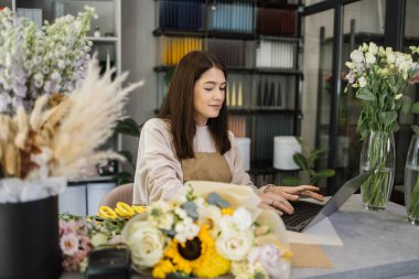 Small family business concept. Caucasian business woman professional designer, florist decorator using laptop at the floral store checking the inventory of shop.