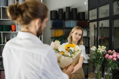 Genç sakallı bir adam, rahat bir çiçekçiden bir kız tatili için güzel bir buket çiçek alır. Çiçekçi dükkanında çiçek buketi yapıyorlar. Küçük işletme.