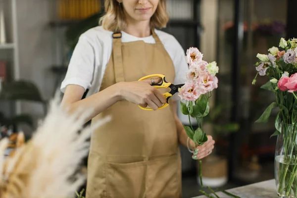 Çiçekçi eski yaprakları keserken dükkânda güzel bir bahar çiçeği buketi yaparken kesilen manzarayı kapat. Modern bayan çiçekçi dükkanda bir iş günü geçiriyor..