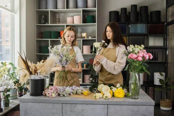 Attractive girls working as florists. Arranging flowers into bouquets and sharing advice with each other. Selling floral gifts in the flower shop.