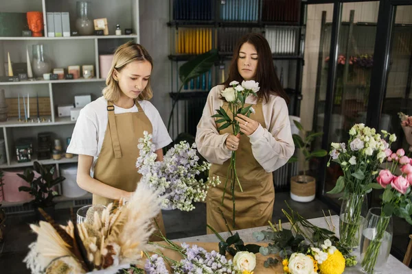 Attractive girls working as florists. Arranging flowers into bouquets and sharing advice with each other. Selling floral gifts in the flower shop.