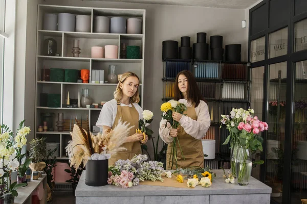 Два Усміхнених Флориста Уніформі Працюють Квітковому Магазині Лічильником Різними Сортами — стокове фото