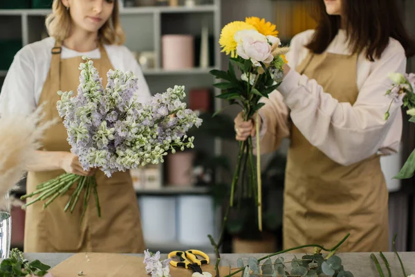 Flowers delivery cropped view. Florists creating order, making bouquet in flower shop. Two female florists are doing bouquets. One woman collecting roses for a bunch, another girl is working too.