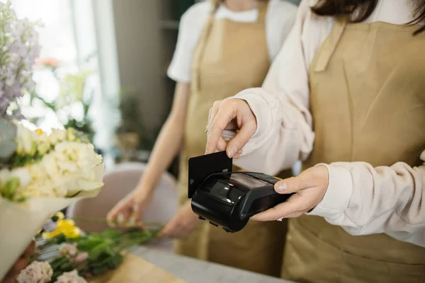 Close up view of hands of young florist female receiving discount card from regular customer and making payment at terminal in flower shop.