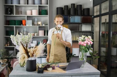 Çiçekçiden güzel bir çiçek kokusu alan yakışıklı bir adam. Çekici sakallı çiçekçi stüdyosunda çiçeklerden bir kompozisyon oluşturuyor..