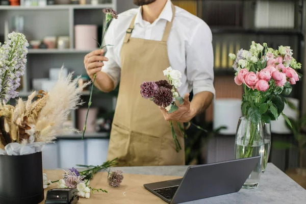 Attractive bearded male gardener in the flower shop make bouquet for a holiday. Family flowers business. Lifestyle flower shop. Beautiful flower composition. Detail. Close up.