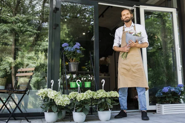 Business man near flower shop door. Photo of handsome man standing in front of flower shop. Male florist outside shop. Woman working at flower shop smiling.