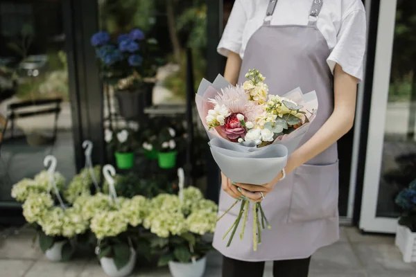 Cropped hands with bouquet near flower shop door. Photo of b woman standing in front of flower shop. Female florist outside shop. Woman working at flower shop.