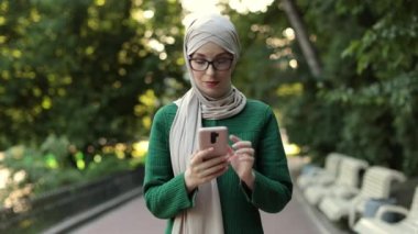 Şehir parkında yürürken cep telefonuyla konuşan neşeli, genç, İslamcı bir iş kadını. Başörtüsü olan güzel genç bir kadın teneffüste akıllı telefon kullanıyor..