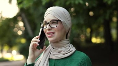 Gülümseyen müslüman bir kadının portresi. Telefon görüşmesi yapıyor. Mola sırasında ek iş alıyor. Parkta yürürken akıllı telefon kullanan tesettürlü neşeli Arap kadın..