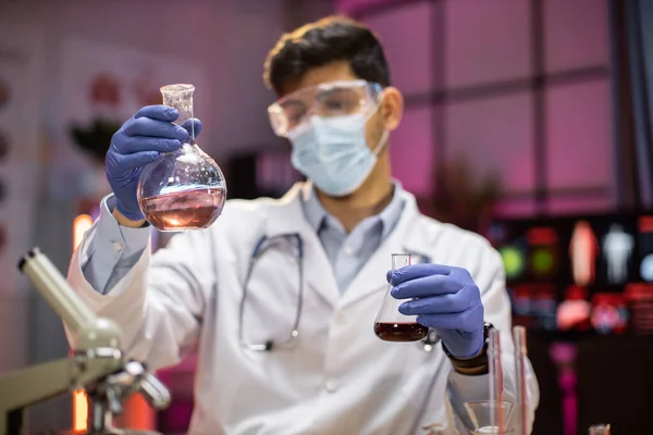 Experienced arab male scientist in health industry doing analysis of substance using microscope. Chemist researcher in sterile lab doing experiments for medical industry using modern technology.