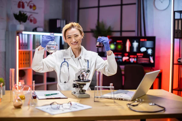 Positive female scientist or medical in lab coat holding test tube with reagent, laboratory glassware containing chemical liquid. Microscope, Biochemistry laboratory research.