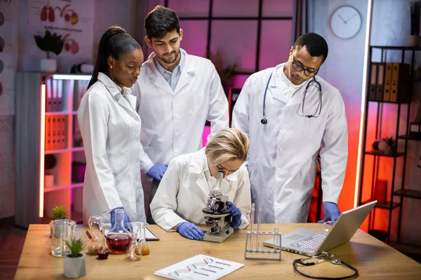 Young Scientist Looking Microscope Laboratory While Her Multinational Colleagues Follow — Zdjęcie stockowe