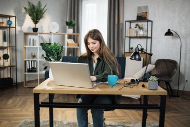 Portrait of beautiful female IT specialist typing on keyboard of modern laptop. Young caucasian woman sitting at workplace with portable computer and document.
