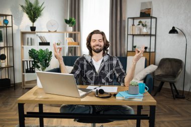 Handsome man freelancer sitting at table with closed eyes and relieving stress by meditation at workplace. Concept of relaxation and harmony, no stress free relief at work.