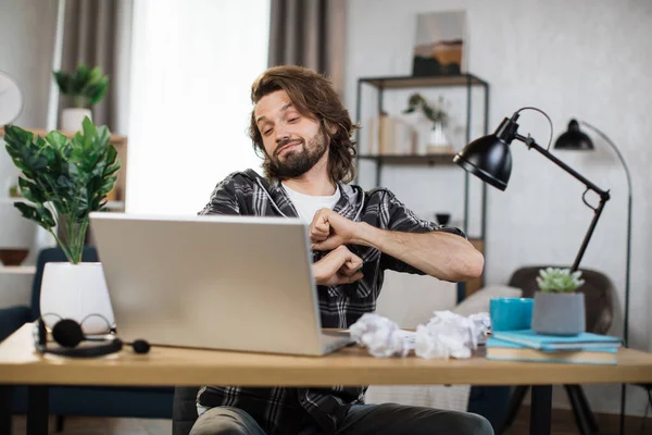 Handsome office man relaxing by stretching his body while sitting in front his computer laptop at the wooden working desk over comfortable living room as background.