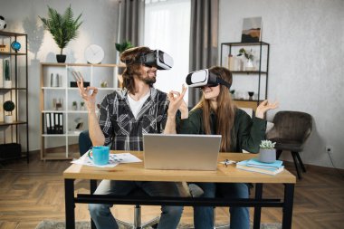 Young people playing games at home, meditating using VR glasses and laptops. Happy family enjoying artificial reality entertaining themselves with innovations.