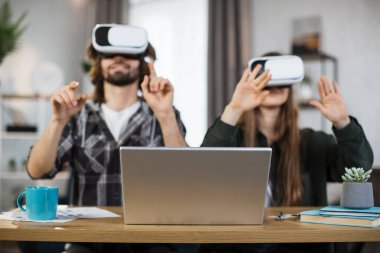 Gündelik giyimli genç çift evde boş vakitlerinde oyun oynamak için VR kulaklık ve dizüstü bilgisayar kullanıyor. Aile ve eğlence kavramı.