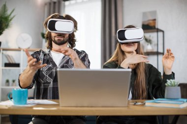 Gündelik giyimli genç çift evde boş vakitlerinde oyun oynamak için VR kulaklık ve dizüstü bilgisayar kullanıyor. Aile ve eğlence kavramı.