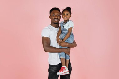 Happy african american man holding little smiling daughter over pink studio background, panorama with free copy space, banner