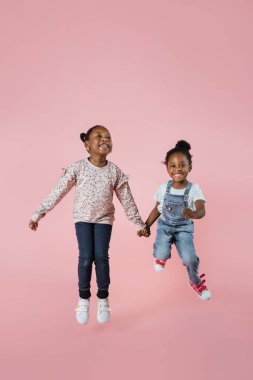 Jumping. Childhood and dream about big and famous future. Pretty little african girls on coral pink studio background. Childhood, dreams, imagination, education, facial expression, emotions concept.