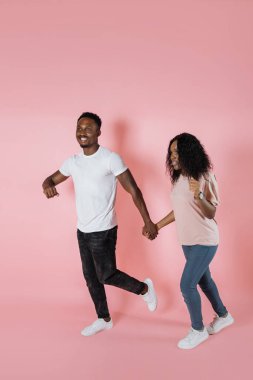 Full length shot of a african american man and woman in casual outfit walking or running together isolated on pink background.