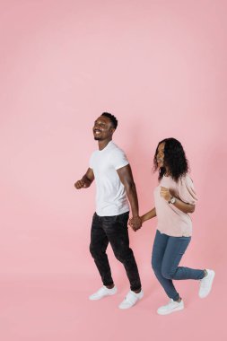 Full length shot of a african american man and woman in casual outfit walking or running together isolated on pink background.