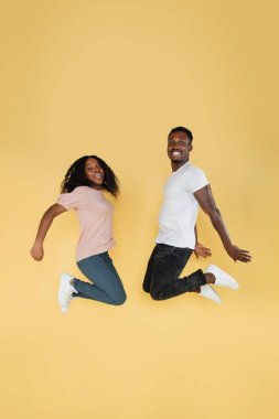 Full length shot of jumping african couple having fun together. Studio photo of young people on yellow background, copy space