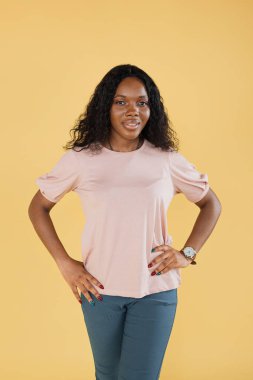 Portrait of young attractive african american woman, wearing pink t-shirt, posing to camera on yellow pastel background. People, races concept.