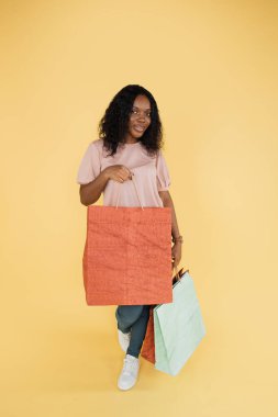 Shopping passion. Portrait of happy excited young african american woman holding shopping bags on yellow background. Sales, black friday, shopping concept.