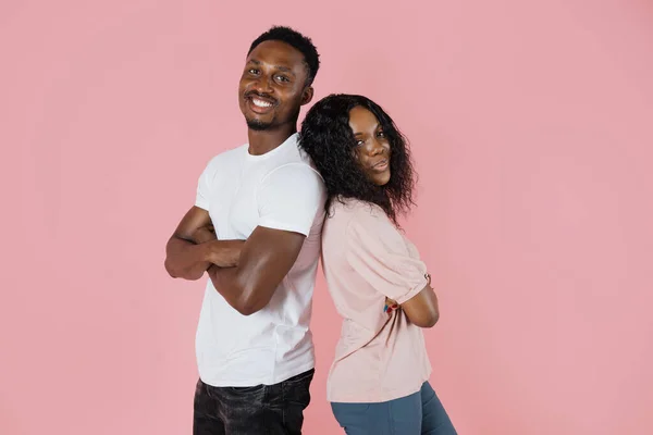 Kind and cheerful. Two african lovers in casual clothes are standing back to back with cheerful facial expressions, posing with folded arms and looking in the camera.