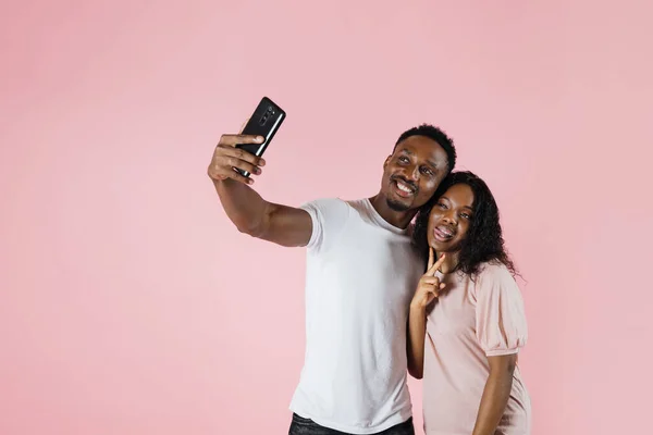 Joyful people using mobile phone to take selfies together in studio. Man and woman taking picture with smartphone and having fun in front of camera. Carefree couple feeling happy.
