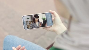 Remote work, e-learning, online lesson. Young muslim woman in park with smartphone, talking with her female office colleague, business partner or studying online during her summer vacations