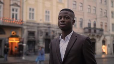 Portrait of handsome african man in stylish suit posing on street of city. Young businessman standing outdoors and looking aside.