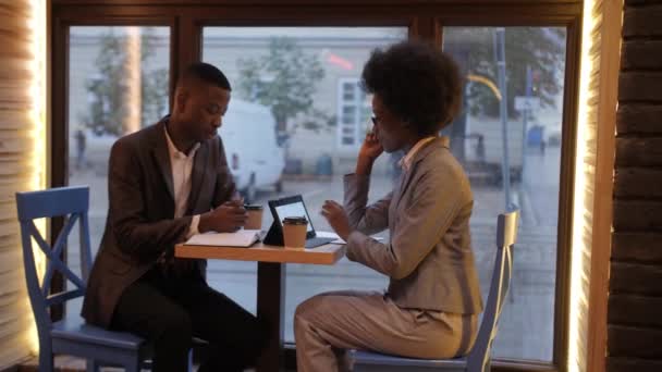 カフェのテーブルでコーヒーを飲みながら 現代のガジェットを使用してコミュニケーションを正式な服でアフロアメリカのビジネスの人々の側のビュー 協力と作業部会の概念 — ストック動画