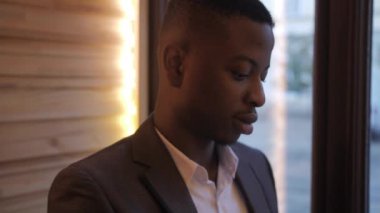 Close up portrait of young african businessman in stylish suit resting during a break. Confident man sitting at cafe table and working on distance.