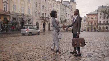 Genç Afro-Amerikan kadın ve sokakta tokalaşan yakışıklı adamın tam boy portresi. Dışarıda birbirini selamlayan iki iş ortağı..