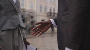 İki Afro-Amerikan ortağının resmi kıyafetleri içinde şehir sokaklarında el sıkışırken. Deri evrak çantası tutan bir adam, elinde pano tutan bir kadın..
