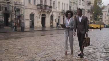 Dosyasıyla güzel bir kadın ve evrak çantalı yakışıklı bir adam sokakta yürüyor ve konuşuyor. Şık giyinmiş iki Afrikalı iş arkadaşı dışarıda poz veriyor..