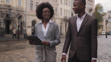 Dosyasıyla güzel bir kadın ve evrak çantalı yakışıklı bir adam sokakta yürüyor ve konuşuyor. Şık giyinmiş iki Afrikalı iş arkadaşı dışarıda poz veriyor..