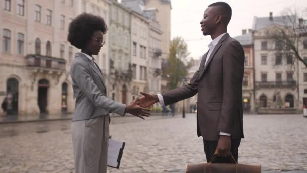 街の通りに立っている間に握手を正式な服で2人のアフロアメリカのパートナー 革のブリーフケースを持った男クリップボードを持った女 — ストック動画