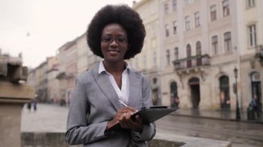 Afro-Afrikalı bir iş kadınının şehrin caddesinde elinde pano tutarken şık kıyafetler giymesi ön planda. Başarılı kariyer kavramı.