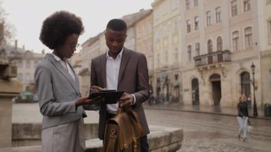 Portrait of two busy african people sign a contract on clipboard while standing on city street. Female assistant make a deal with male employer.