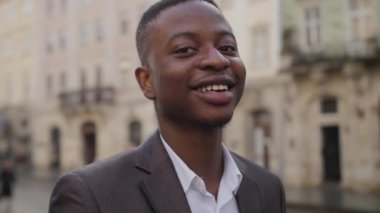 Close up portrait of young african man in business suit outdoor on old fountain of city street. Urgent work online. Break, relax concept.