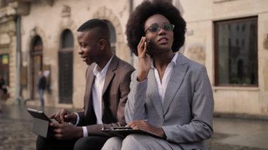 Yakışıklı takım elbiseli adam dijital tablet üzerinde çalışırken çekici kadın cep telefonuyla konuşuyor ve panoya yazı yazıyor. Ofis dışındaki sorunları çözen iki Afrikalı meslektaşım..